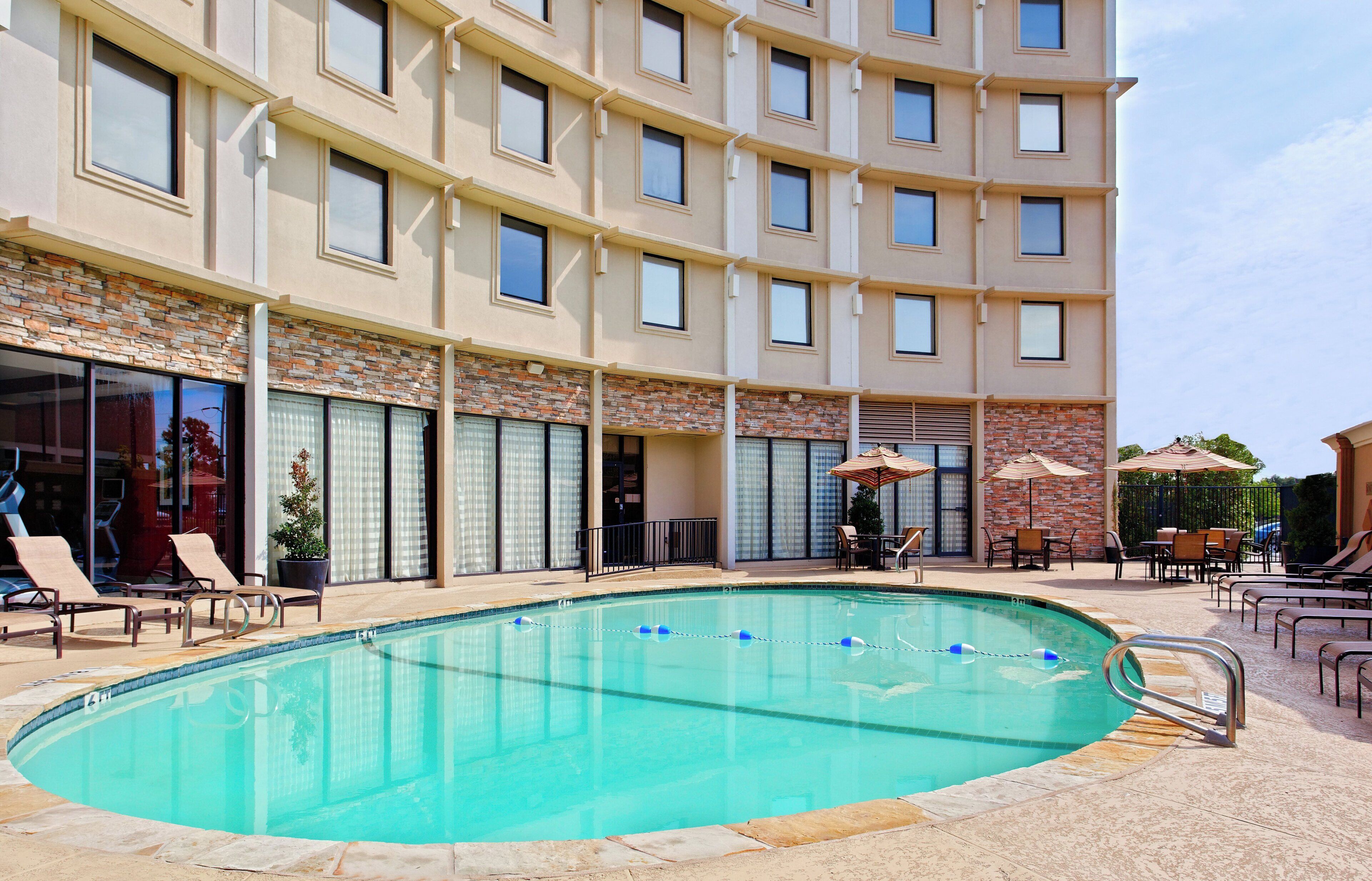 Un espace piscine d’hôtel comprenant une piscine à eau claire, des chaises longues et des parasols.