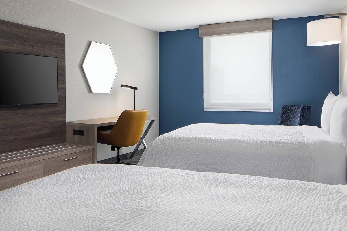 A hotel room with two beds, a desk, a chair, a TV, and a window with a view.