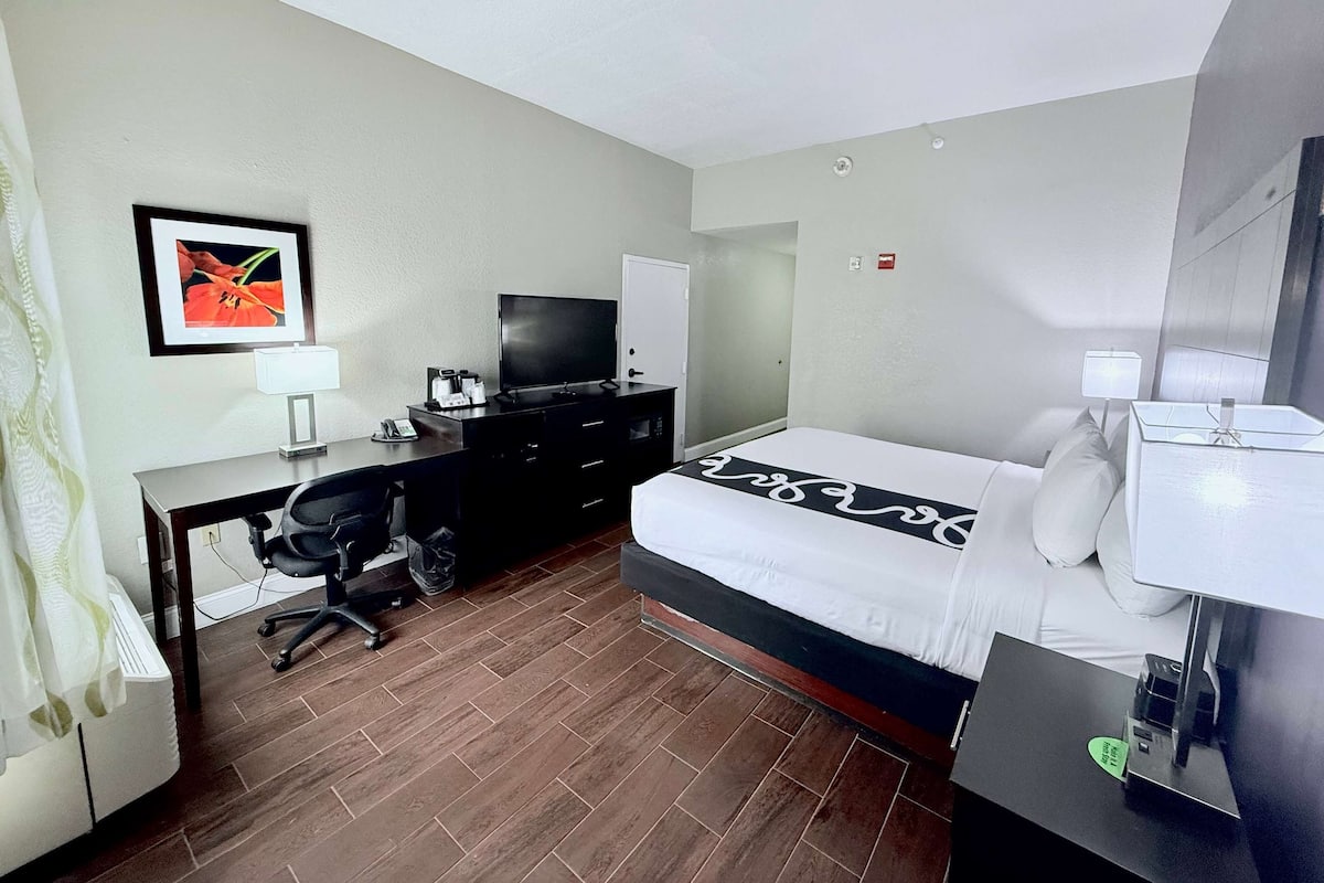 Een hotelkamer met een bed, bureau, stoel, televisie en een ingelijst schilderij aan de muur.