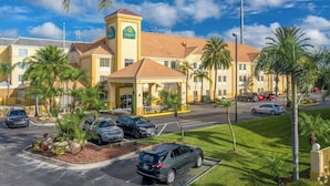 A hotel with a central tower, multiple parking spaces, and palm trees. - La Quinta Inn & Suites by Wyndham Orlando Universal area (Orlando)