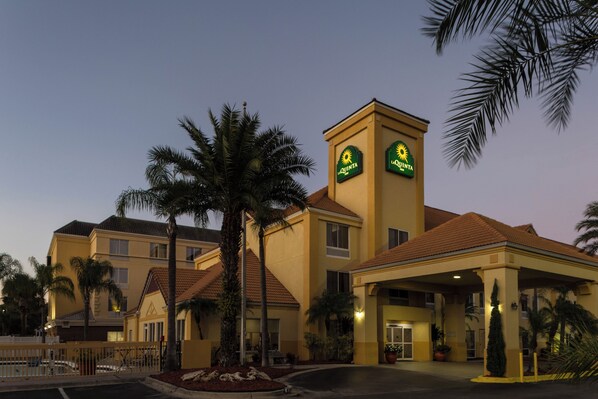 A hotel with a prominent 'Quinta' sign, a covered entrance, and a palm tree in the foreground. - La Quinta Inn & Suites by Wyndham Orlando Universal area (Orlando)