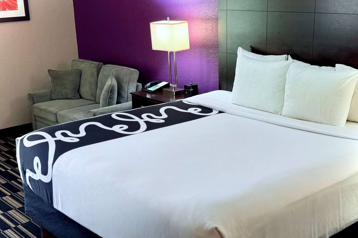 Een hotelkamer met een bed, nachtkastje, lamp, stoel en een paarse muur.