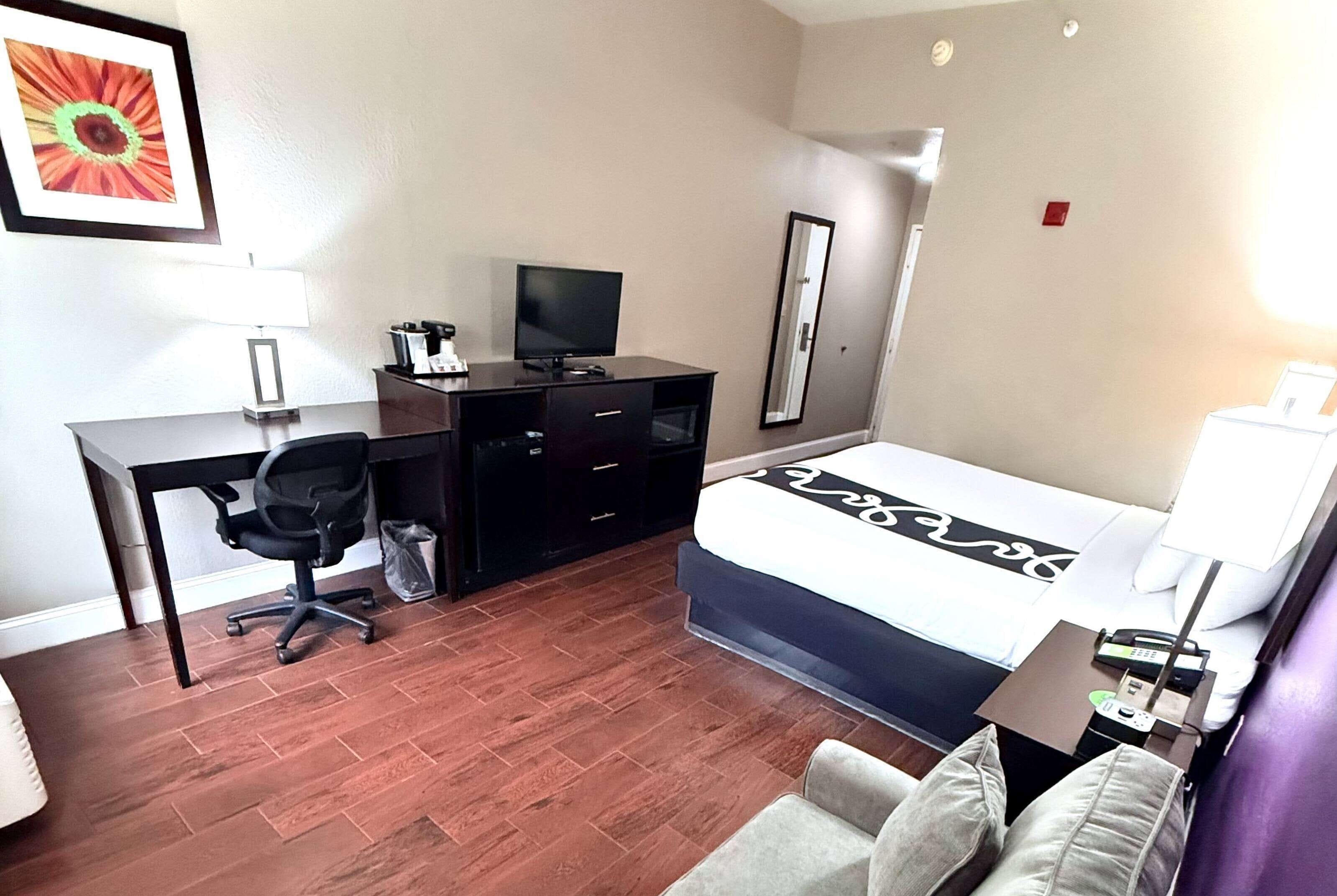 A hotel room with a bed, a desk with a computer, a chair, a TV, and a mirror.