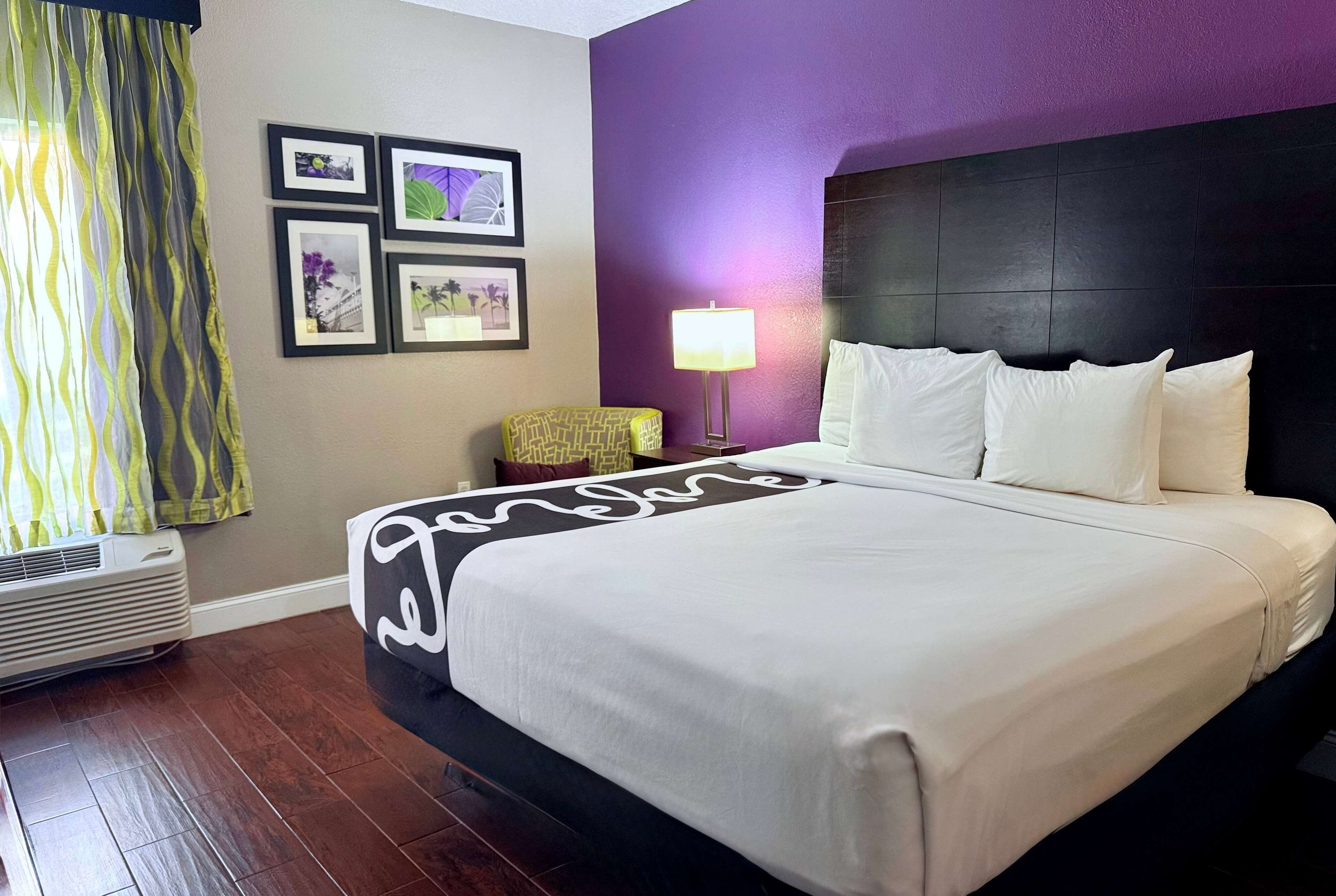 Una habitación de hotel con una cama grande, aire acondicionado montado en la pared y una ventana con cortinas.