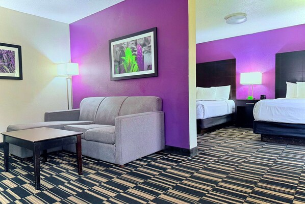 A hotel room with a sofa, a small table, a bed, and a nightstand with a lamp. - La Quinta Inn & Suites by Wyndham Orlando Universal area (Orlando)