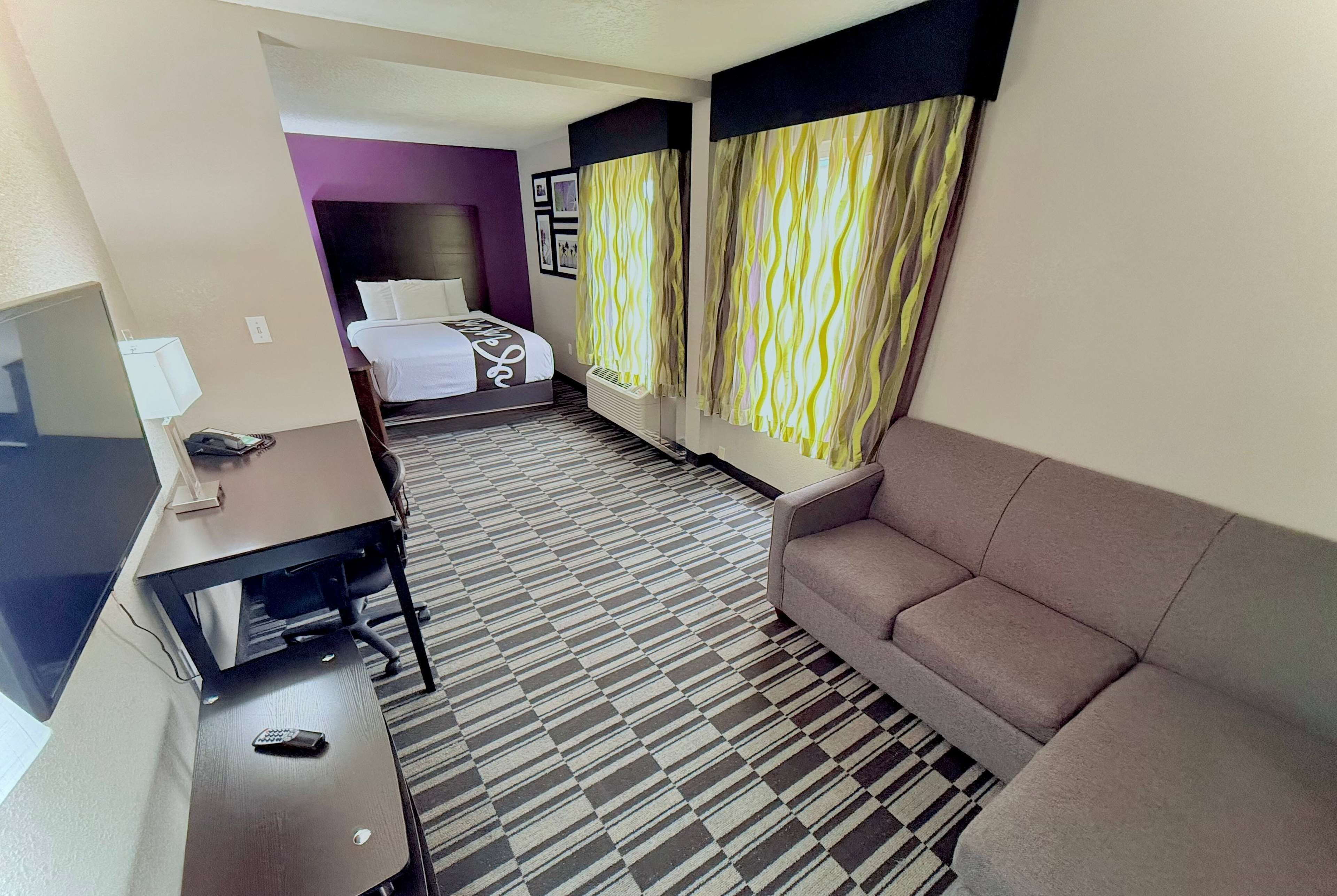 A hotel room with a bed, a sofa, a desk with a computer, and a TV.