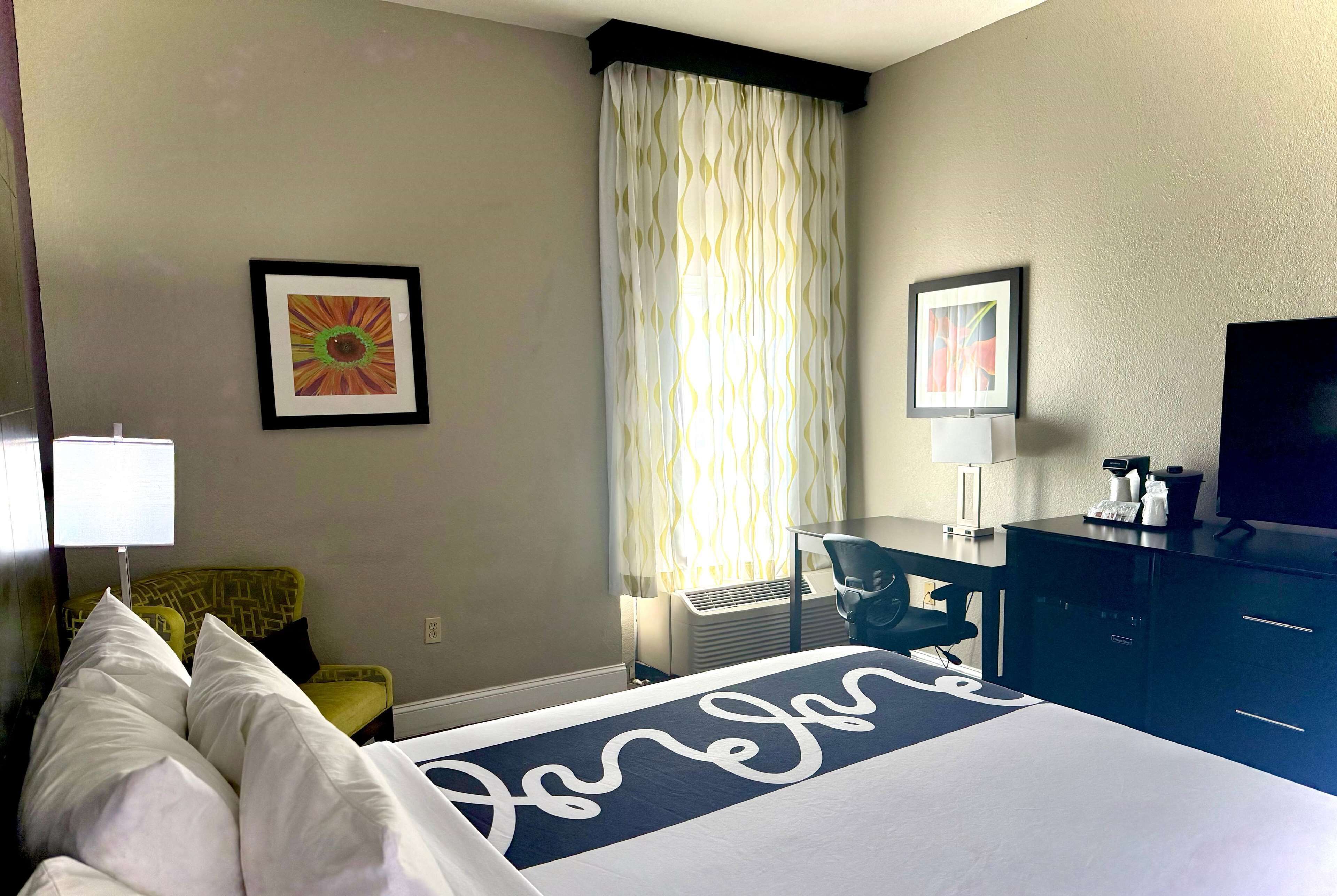 A hotel room with a bed, a desk, a chair, a television, and a window with curtains.