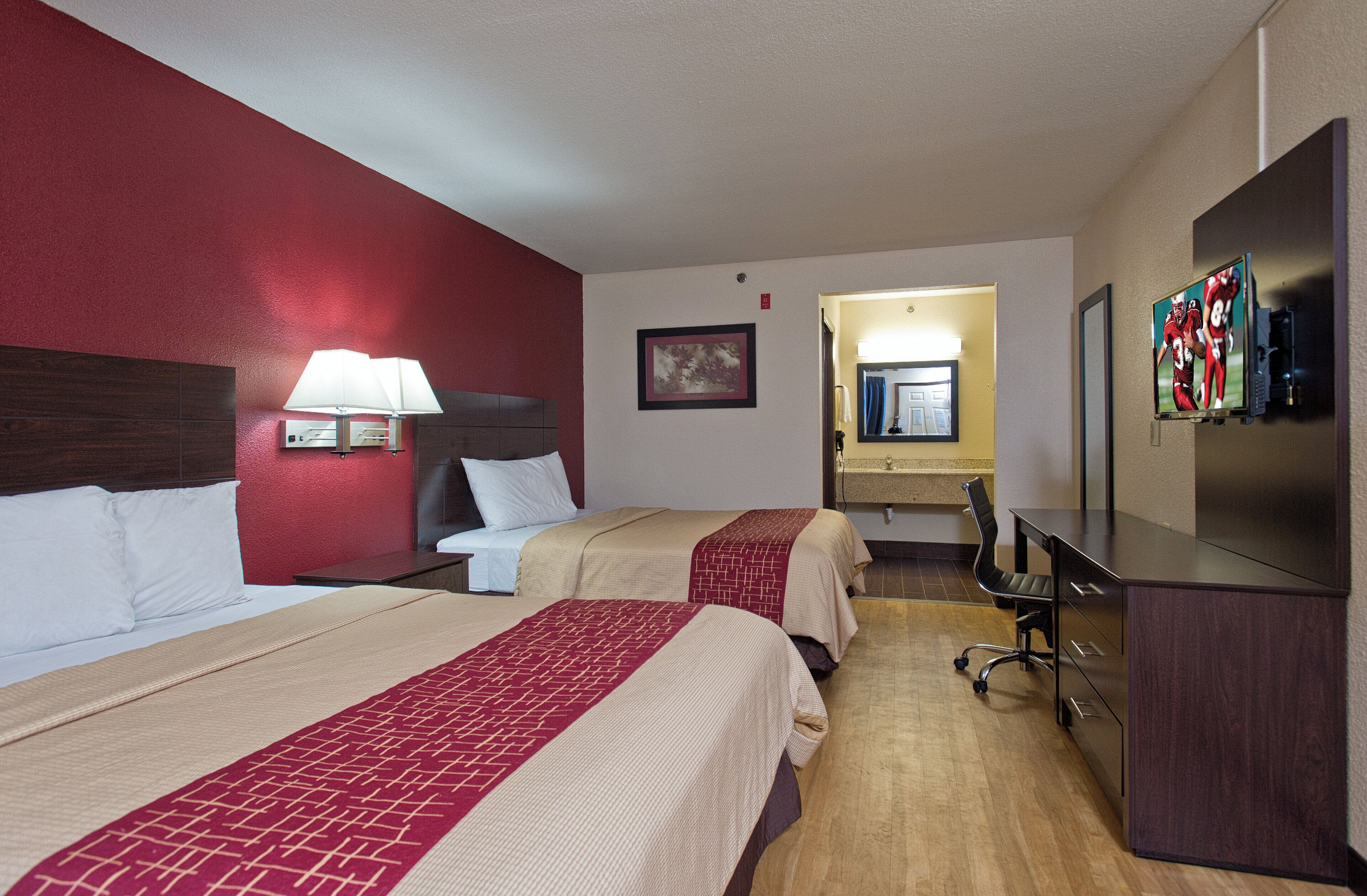A hotel room with two beds, a desk, a television, and a bathroom visible through an open door.
