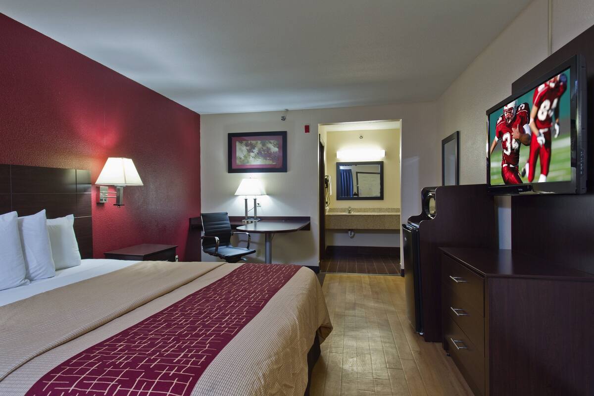 Ein Hotelzimmer mit Bett, Schreibtisch, Stuhl, Fernseher und Spiegel.