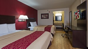 Een hotelkamer met twee bedden, een bureau, een stoel, een televisie en een badkamer op de achtergrond.