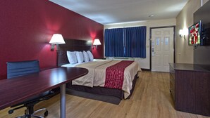 Een hotelkamer met een bed, een bureau, een stoel, een televisie en een deur.