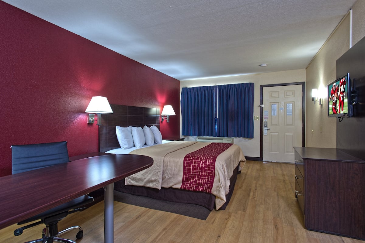 Ein Hotelzimmer mit einem Bett, einem Schreibtisch, einem Stuhl, einem Fernseher und einer Tür.