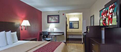 A hotel room with a bed, a desk, a chair, a television, and a bathroom visible through an open door.