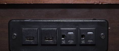 A black electrical outlet with four USB ports and two standard electrical outlets on a wooden surface.