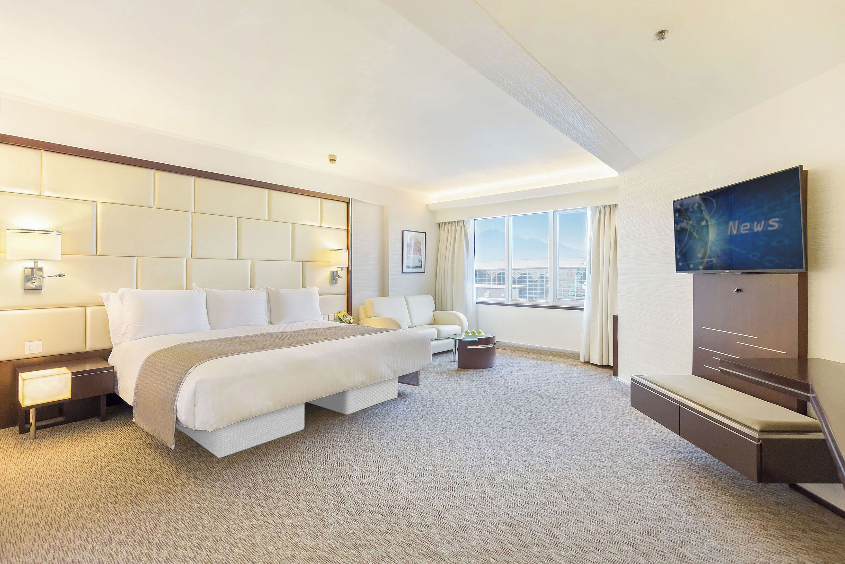 A hotel room with a large bed, a sofa, a TV, and a view of the city.