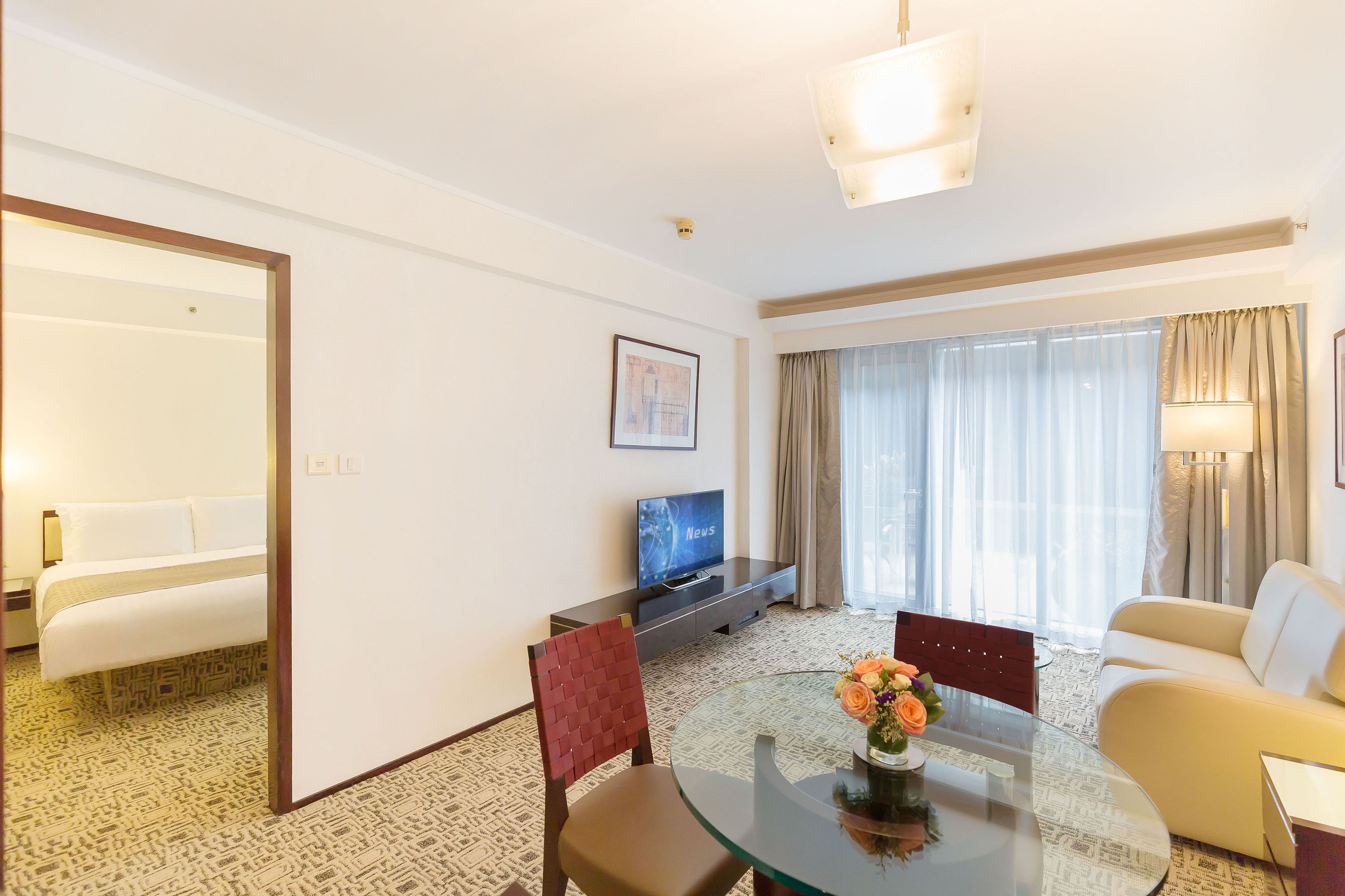 A hotel room with a bed, a TV, a dining table with chairs, and a sofa.