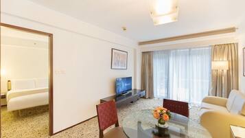 A hotel room with a bed, a TV, a dining table with chairs, and a sofa.