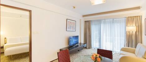 A hotel room with a bed, a TV, a dining table with chairs, and a sofa.