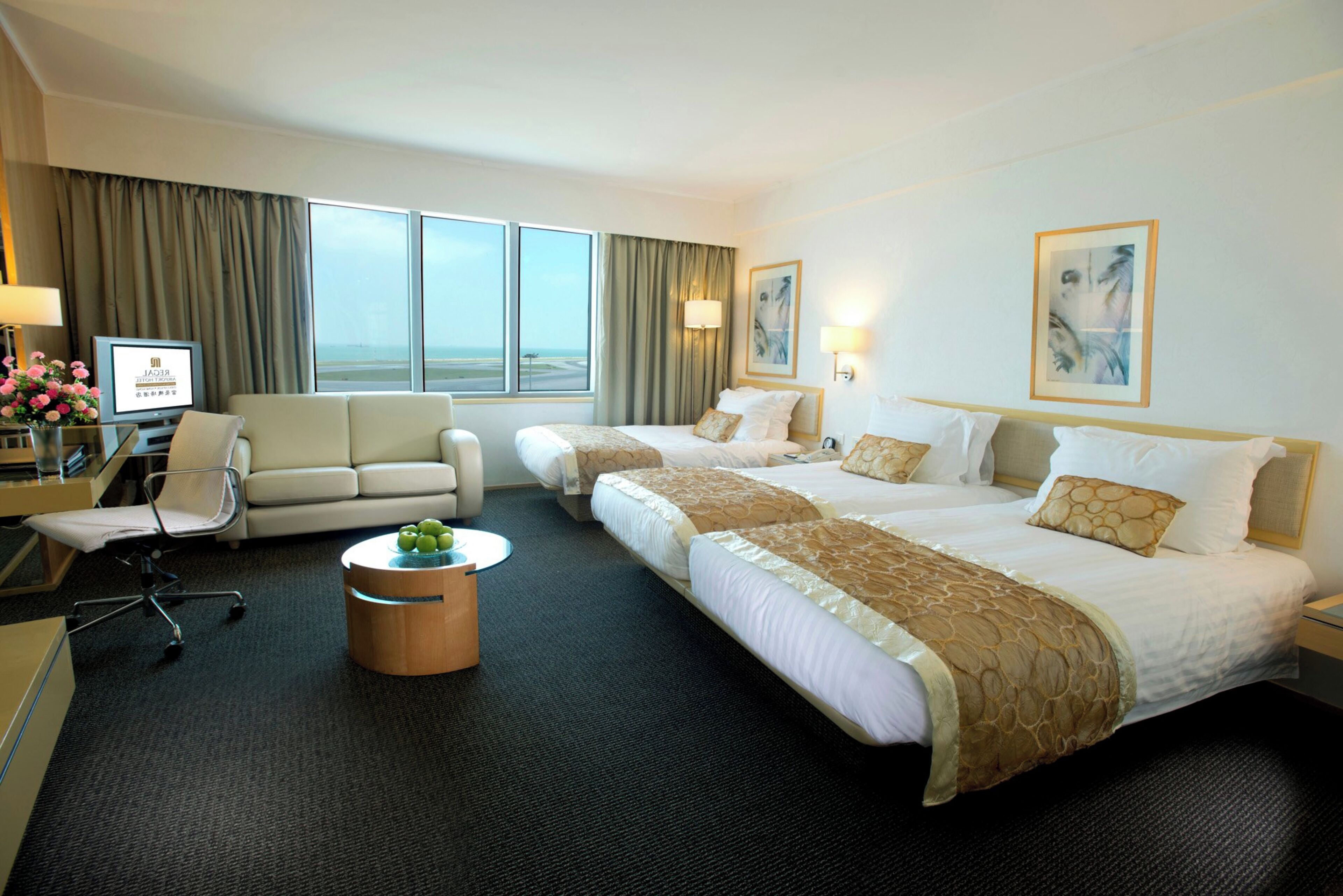 A hotel room with two beds, a sofa, a desk with a computer, and a view of the airport.