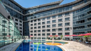 A modern hotel with a large indoor swimming pool, multiple floors, and red umbrellas for shade. - Regal Airport Hotel (Chek Lap Kok)