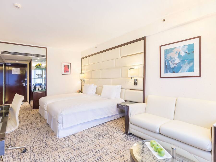 A hotel room with a large bed, a white sofa, a desk with a chair, and a small table with apples.