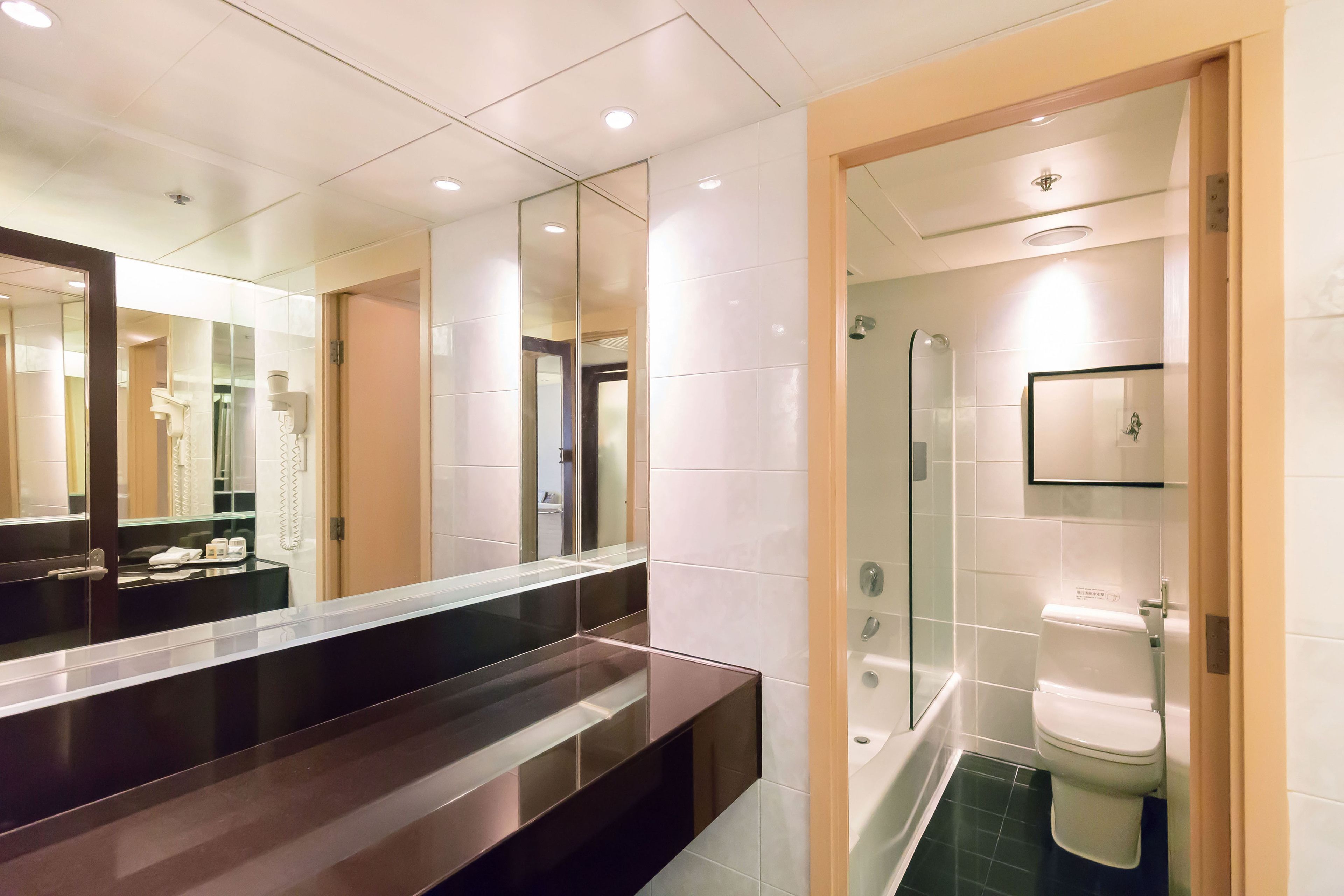 A modern bathroom with a dark countertop, a large mirror, a glass shower enclosure, and a white toilet.