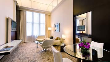 A hotel room with a glass dining table, a sofa, a TV, and a large window with curtains.
