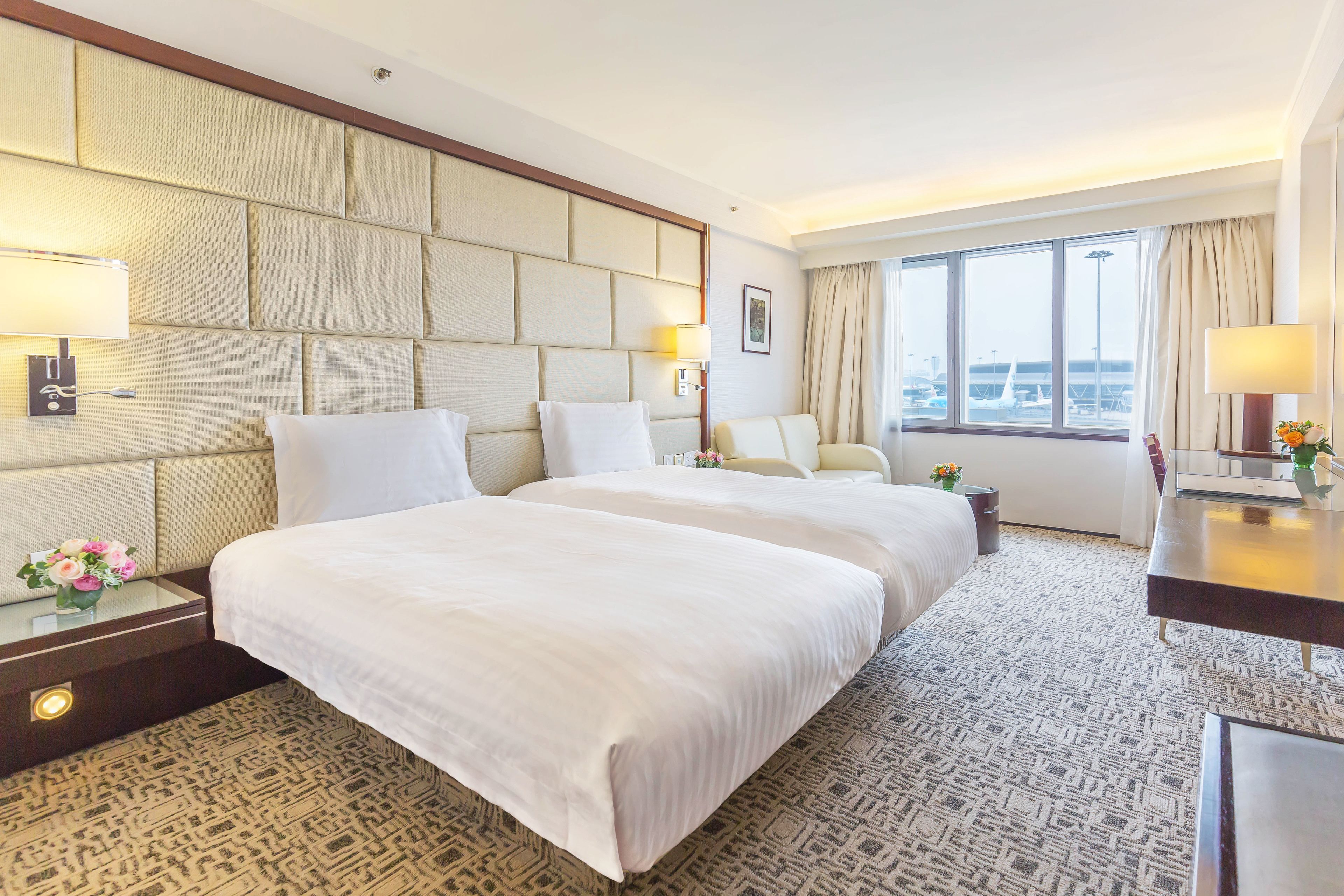 Une chambre d’hôtel avec deux lits, un bureau et une vue sur l’aéroport.