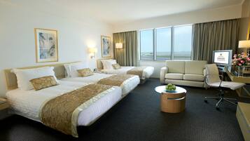 A hotel room with two beds, a sofa, a desk with a computer, and a view of the outdoors.