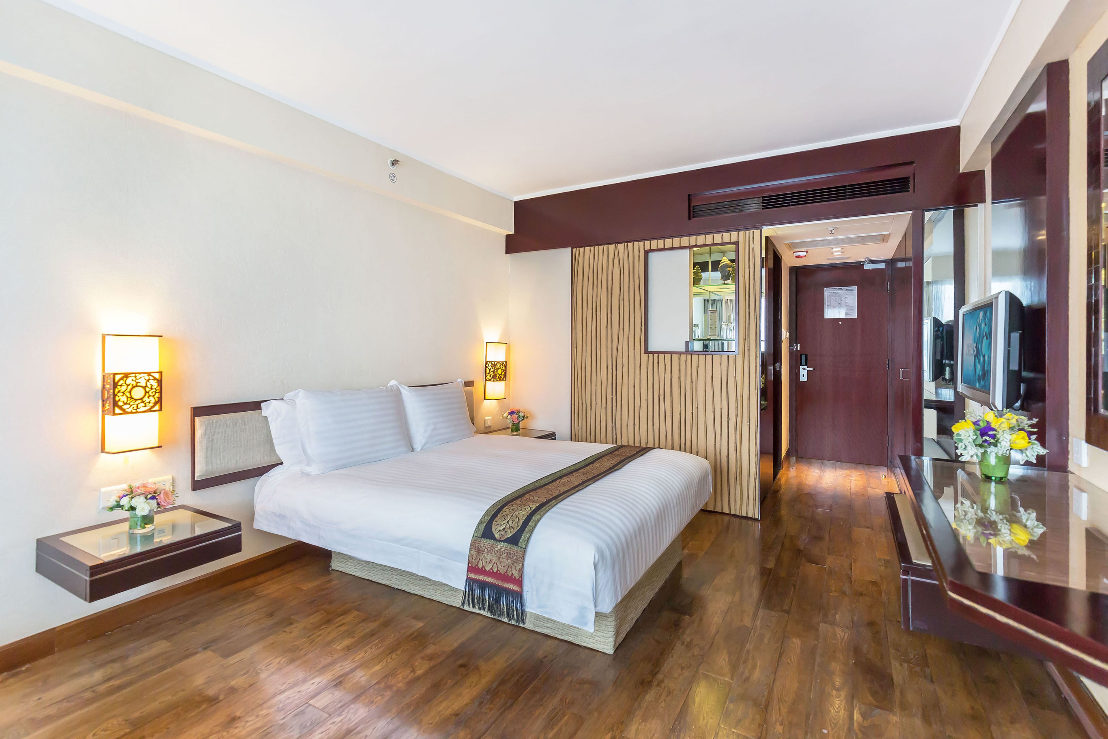 A hotel room with a large bed, bedside tables with lamps, a mirror, and a wooden floor.