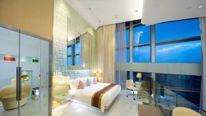 A modern hotel room with a large bed, a glass partition, a seating area, and a view of the city at night. - Regal Airport Hotel (Chek Lap Kok)