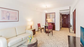 A hotel room with a sofa, a small table with a vase of flowers, a chair, a desk, and a television.