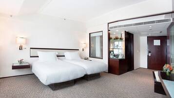 A hotel room with a large bed, bedside tables with lamps, a mirror, a small desk with a chair, and a view of the bathroom.