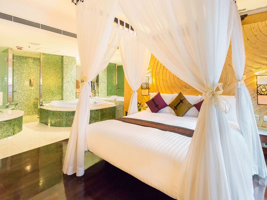A spacious bedroom with a large bed, a sitting area, and a bathroom with a green mosaic wall.