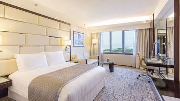 A hotel room with a large bed, a desk, a chair, a small table, and a large window offering a view.