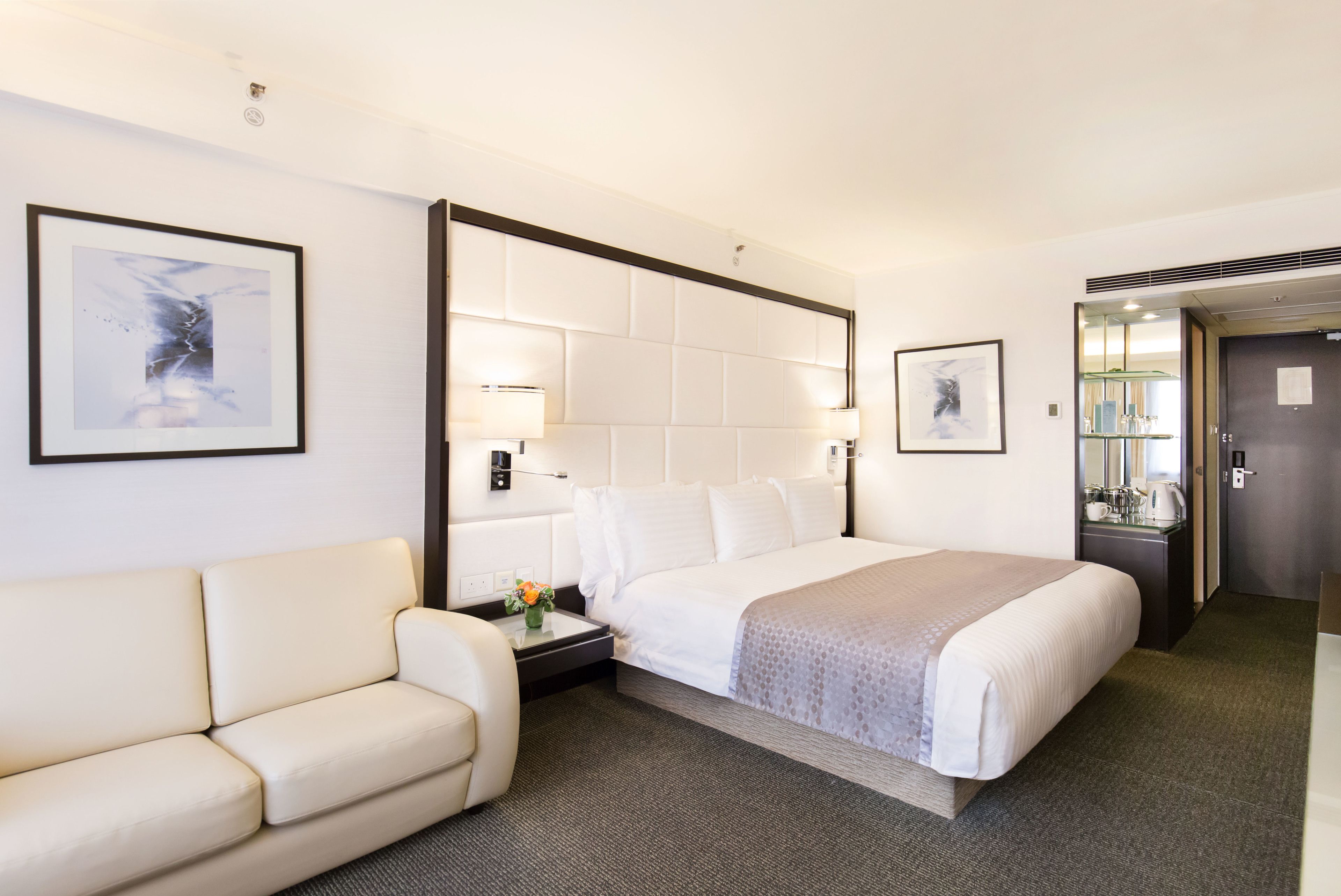 Habitación de hotel con una cama grande, un sofá, una mesita de noche con lámpara y cuadros en las paredes.