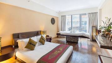A hotel room with a large bed, a bedside table, a nightstand, a window with curtains, and a view of the city.