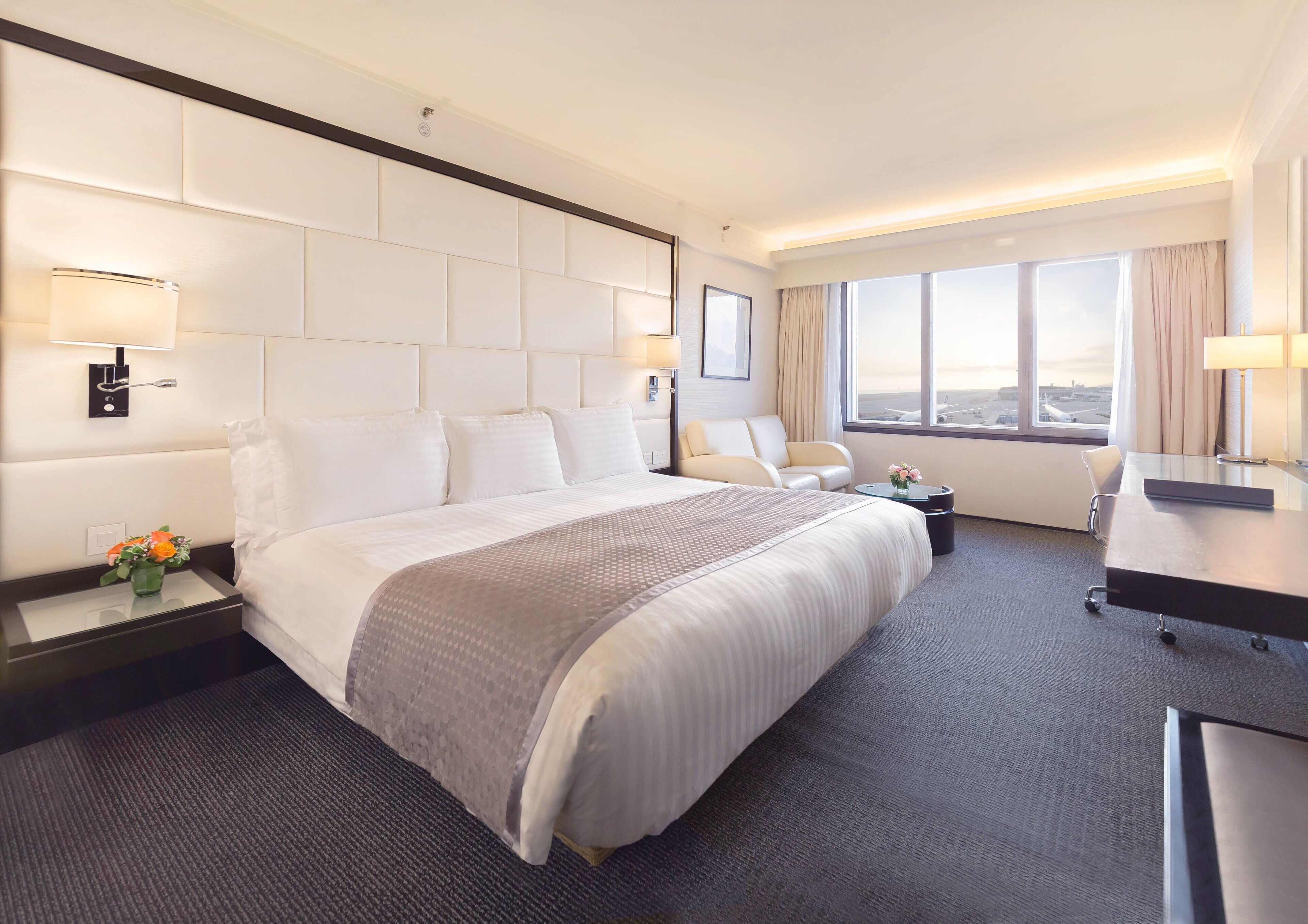 Un cuarto de hotel con una cama grande, un escritorio, una silla y vista a la ciudad por la ventana.