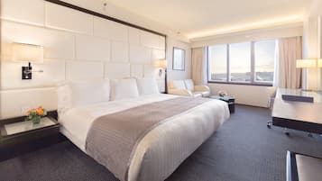 Un cuarto de hotel con una cama grande, un escritorio, una silla y vista a la ciudad por la ventana.