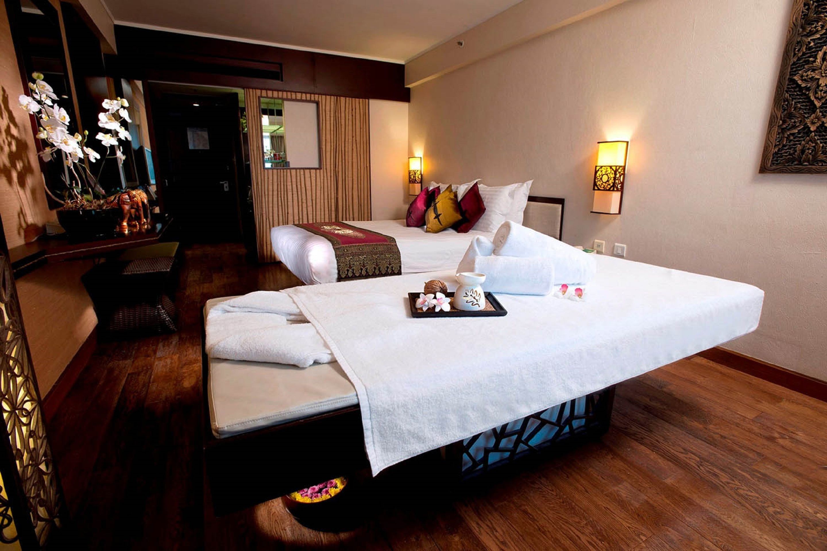 A hotel room with a large bed, a small sofa, a massage table, and a decorative plant.