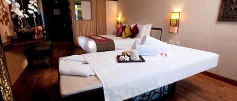 A hotel room with a large bed, a small sofa, a massage table, and a decorative plant.