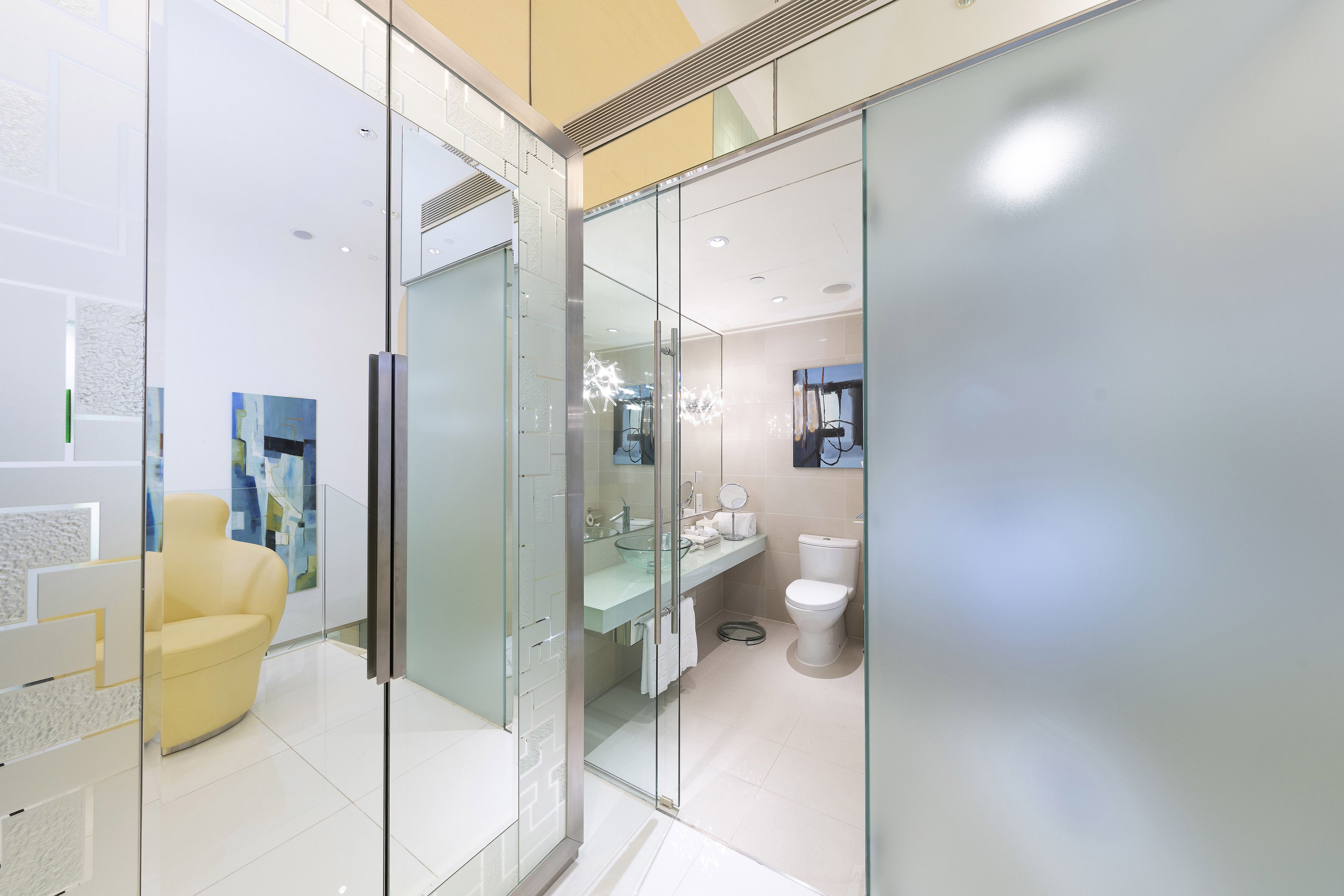 A modern bathroom with a glass partition, a yellow chair, and a toilet.