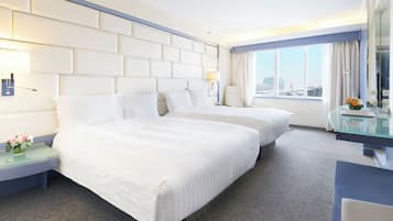 A hotel room with two beds, a glass desk, a nightstand, and a view of the city.