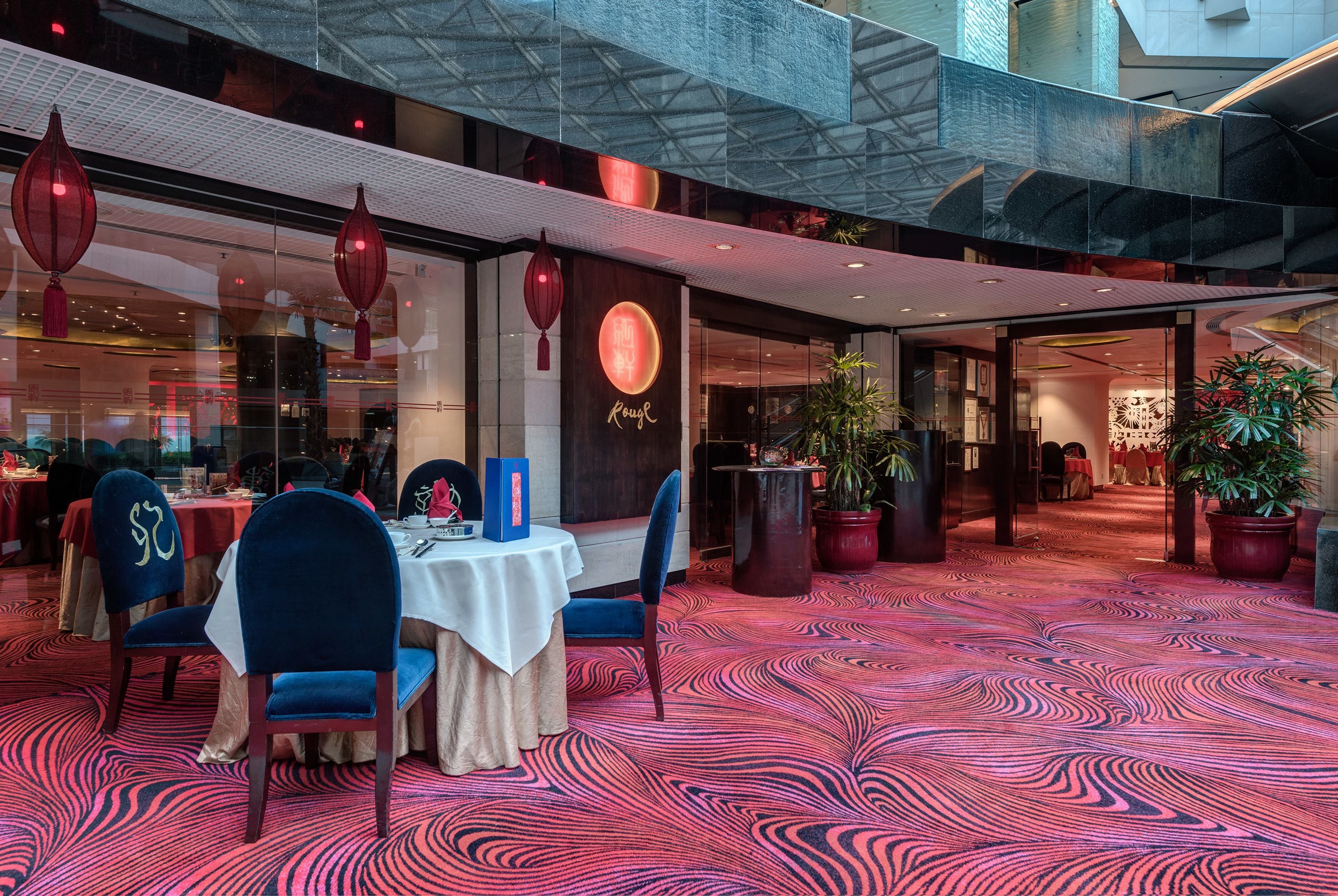 A restaurant with a red patterned carpet, blue chairs, and a table with a white tablecloth.