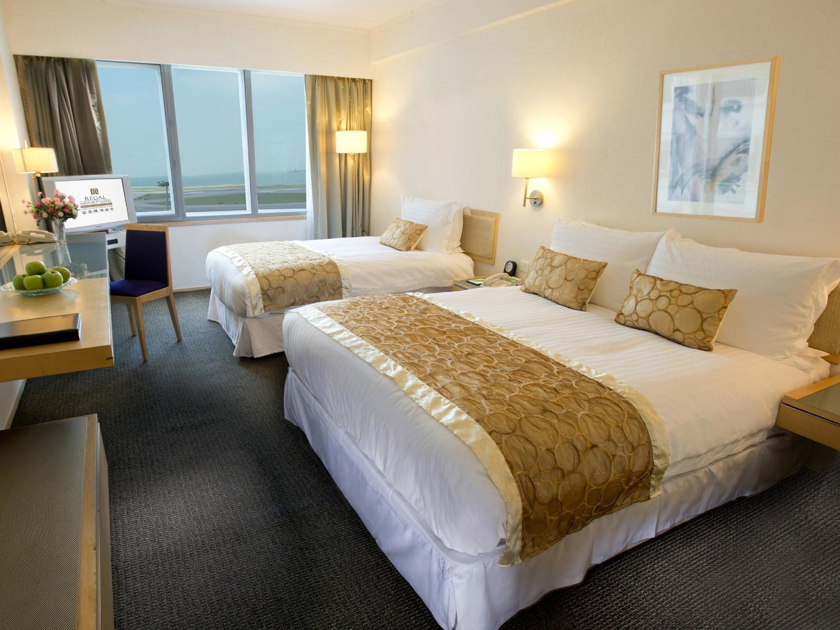 A hotel room with two beds, a desk with a phone, a chair, and a view of the sea.