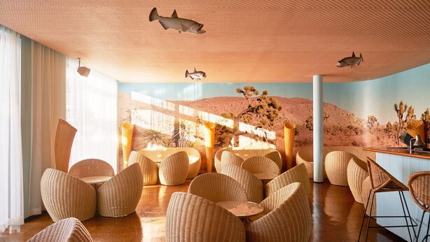 Um quarto espaçoso com cadeiras de vime e um mural com paisagem de deserto.