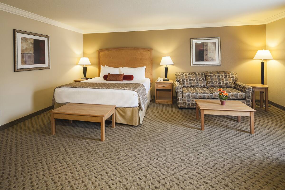 Ein Hotelzimmer mit Bett, Sofa, Couchtisch und zwei Lampen.
