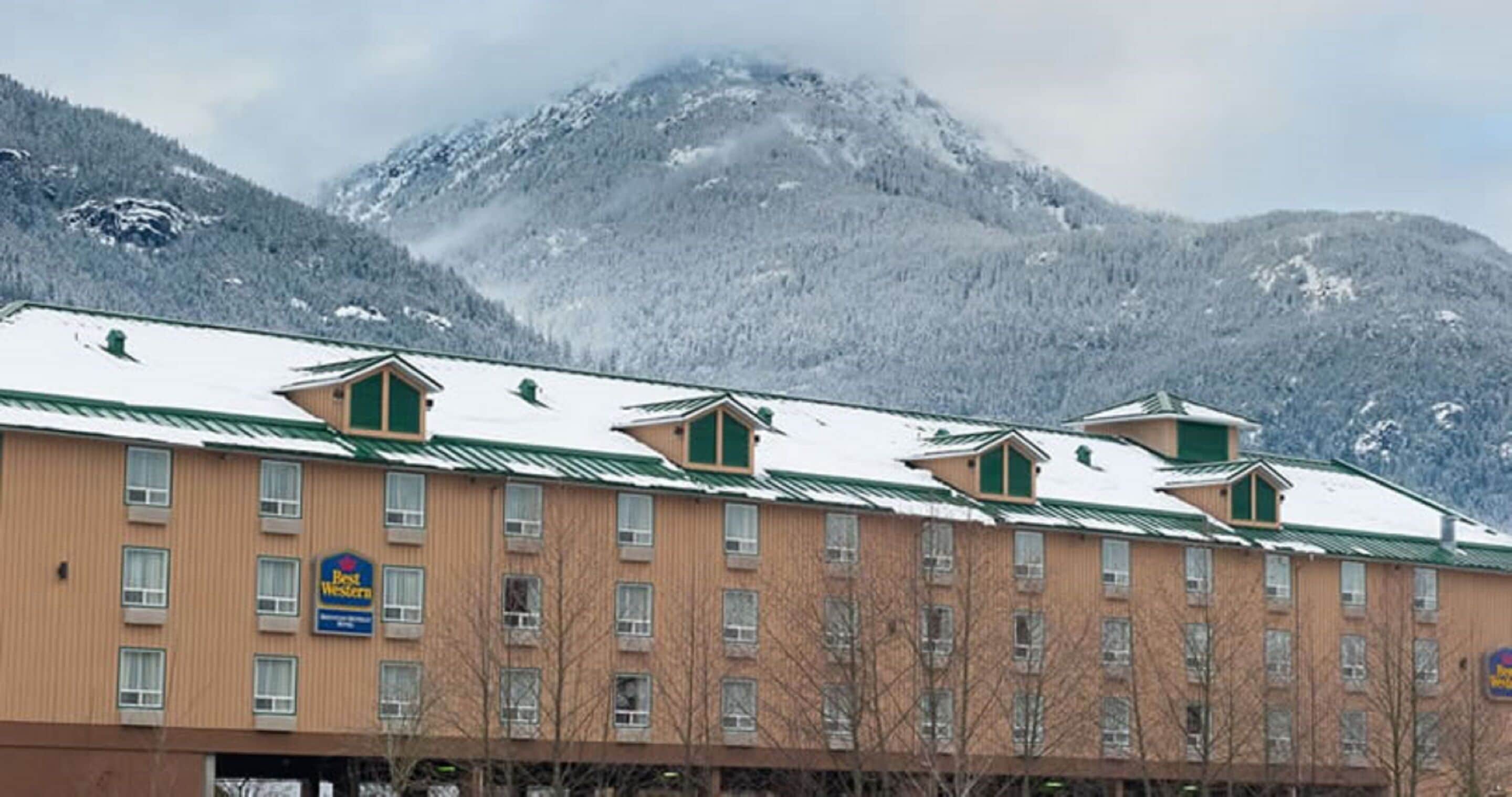 Um hotel com uma fileira de quartos, placa Best Western e montanhas ao fundo.