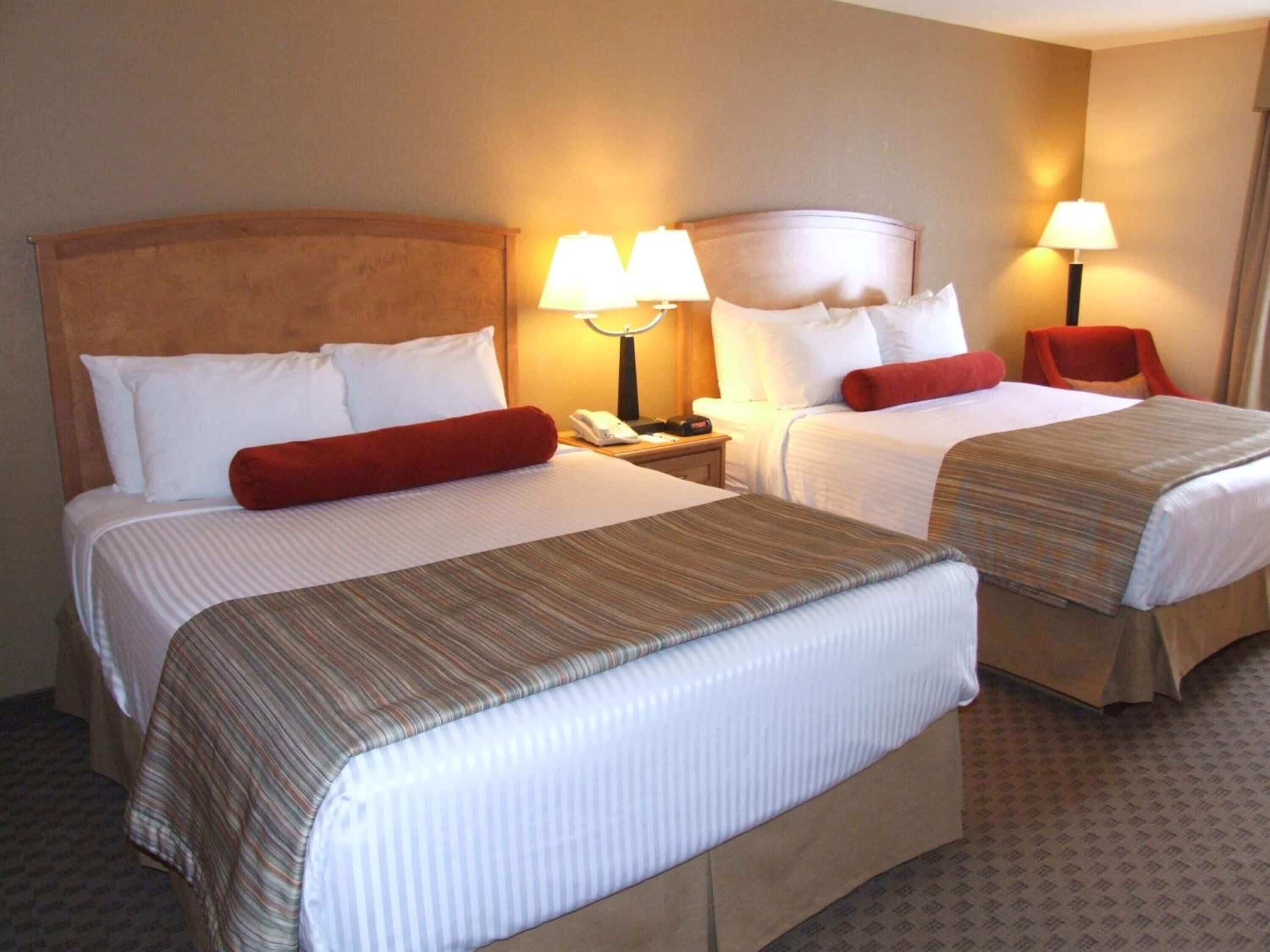 A hotel room with two beds, each with a headboard, bedside lamps, and a telephone on the nightstand.