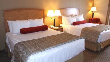 A hotel room with two beds, each with a headboard, bedside lamps, and a telephone on the nightstand.